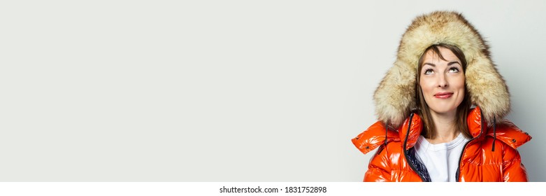 Young Girl In A Red Jacket And A Fur Hat, Smiles Up On A Light Background. Fashion Concept, Trend. Baner