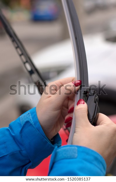 Young girl with red nails is preparing to put\
a new car windshield wiper brush to replace the old wiper blade\
vertical orientation