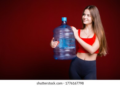 A young girl in a red shirt and long hair smiles and holds a large blue gallon on a red background. Purified Water Concept.