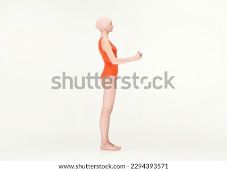 Young girl in red swimsuit and swimming cap standing with hands holding together isolated over white background. Side view. Concept of retro style, sport, fashion, youth, vintage. Copy space for ad