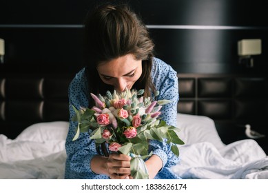 Young girl rejoices at the presented bouquet of flowers. A woman in a blue dress sits on the bed and sniffs roses. The concept of wedding, flower delivery and love.