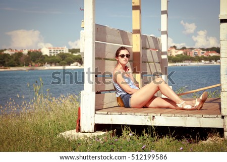 Young Girl Relaxing by the Sea. Beautiful Slim Woman in Sunglasses Resting Outdoors. Summer Vacation. Retro Toned Photo.