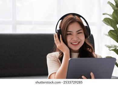 Young Girl Relaxing in Modern Living Room with Headphones and Tablet, Enjoying Music or Online Content, Bright and Cozy Home Interior with Natural Light and Green Plant in Background - Powered by Shutterstock