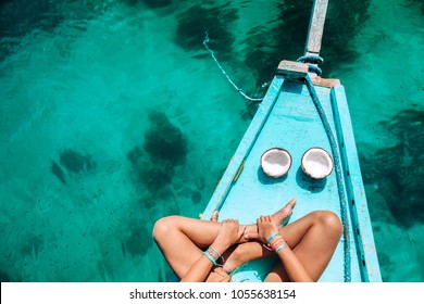 Young girl relaxing on the boat and eating coconut over clear sea water, top view. Travelling tour in Asia: El Nido, Palawan, Philippines.