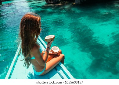 Young girl relaxing on the boat and eating coconut over clear sea water. Travelling tour in Asia: El Nido, Palawan, Philippines.