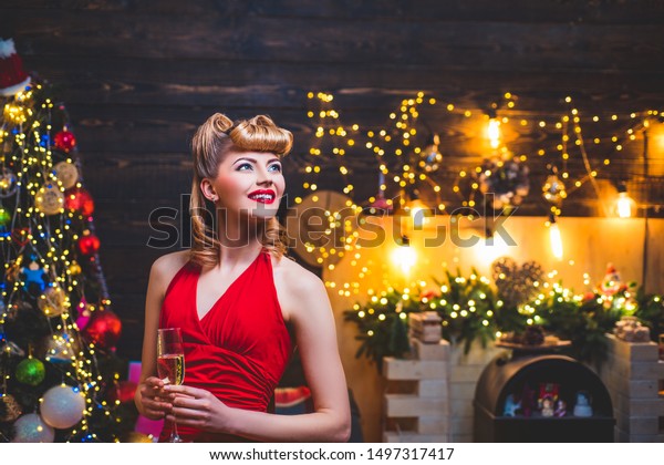 Young girl with retro hairstyle and pinup makeup over Christmas tree. Christmas Party drinks and holidays people concept. New year fashion clothes
