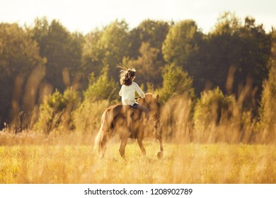 Young girl is riding a sorrel horse in a field, far away, back view