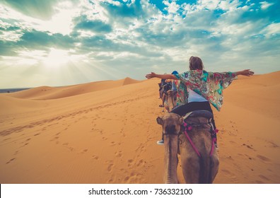 Young girl rising arms while riding camel in the middle of the desert