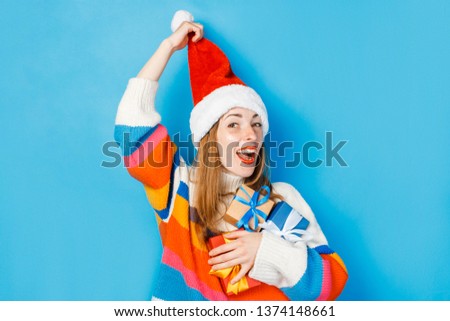 A young girl in a Santa Claus hat is holding gift boxes on a blue background. The concept of New Year and Christmas, gifts for the winter holidays, shopping at sales.