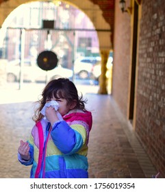 A Young Girl Scrunches Up Her Face And Wipes Her Nose With A Tissue. 