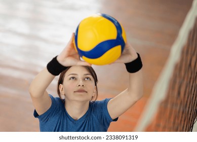 Young girl setting the ball over the net before hitting it. Pupil of high school practicing volleyball skills, PE lesson at school in the gym - Powered by Shutterstock