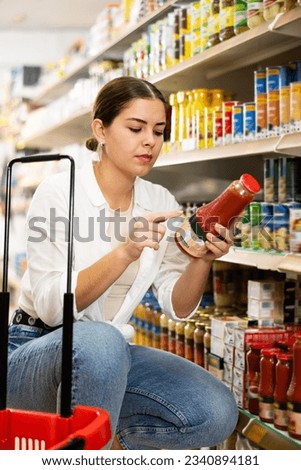 Young girl shopping in supermarket, choosing natural juices and reading labels on bottles with interest