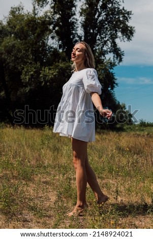 A young girl in a short dress stands in nature with her arms spread