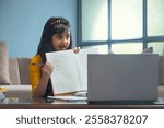 Young girl showing the spellings of the words her teacher dictated in front of the laptop during online class