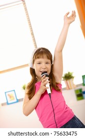 Young Girl Singing Into Microphone With Arm Raised High, Looking At Camera.?