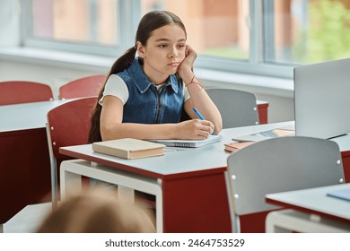 A young girl sits at a desk, with bored face expression in school - Powered by Shutterstock