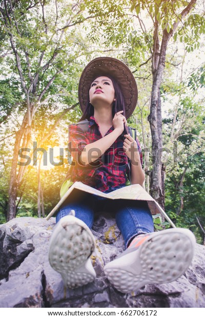 The young girl sits on nature park with map and looks\
at the forest . asia women  tourists. the traveler looks for the\
road on the map