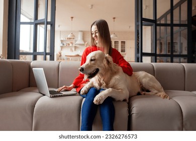 young girl sits on sofa with dog and uses laptop at home, woman with golden retriever looks at the computer and smiles - Powered by Shutterstock