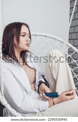 A young girl sits and smokes an electronic cigarette.