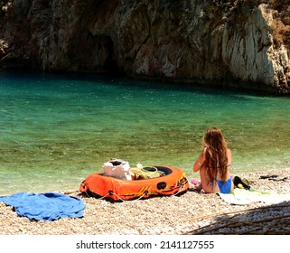 A Young Girl Sitting By The Sea. Long Blond Hair And A Glucose Monitor On Her Arm