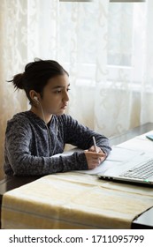 Young Girl Sitting At The Dining Table With Laptop At Home Schooling, Online Virtual Classroom Video Conference, Distant Education. Active Participation At The Lesson With Earphones, Doing Homework.