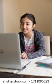 Young Girl Sitting At The Dining Table With Laptop At Home Schooling, Online Virtual Classroom Video Conference, Distant Education. Active Participation At The Lesson With Earphones, Doing Homework.