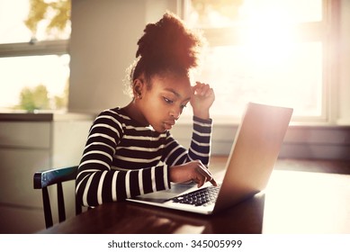 Young girl sitting at the dining table at home working on her homework from school typing out an answer on a laptop computer, e-learning concept