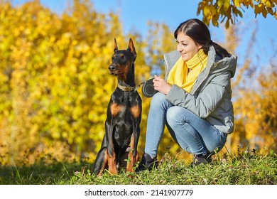 young girl is sitting with her dog Doberman. photo shoot on an autumn background.