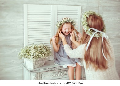 A young girl is sitting on the fireplace. Her mother is tiding her hair. They are both having floral wreathes and casual clothes on. The atmosphere of happiness is all around them. - Powered by Shutterstock