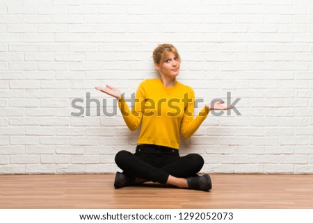 Young girl sitting on the floor making unimportant gesture while lifting the shoulders