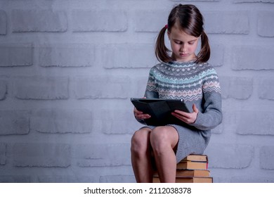 Young Girl Sitting On Stack Of Books With PC Tablet. Concept Of Learning New Knowledge, Self Improvement And Development Of Mental Abilities