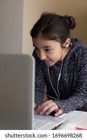 Young girl sitting at the table with laptop at home schooling, online virtual classroom video conference, distant education. Happy child enjoying e-learning, chatting with friends over internet. - Shutterstock ID 1696698268