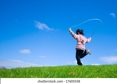 Young girl skipping on the green grass in the beautifull blue sky background