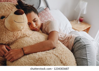 Young girl sleeping with her arms around a big teddy bear on bed. Girl sleeping on bed hugging a brown teddy bear.
