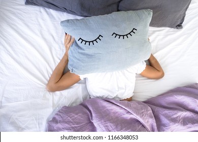 A Young Girl Sleeping In White Bed Does Not  Want To Get Up Early In The Morning,covering Her Face With A Pillow With Closed Eyes On It.