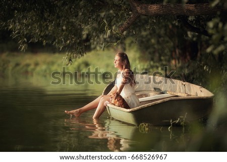 Young girl with a small dog in a boat on the lake in the rays of light