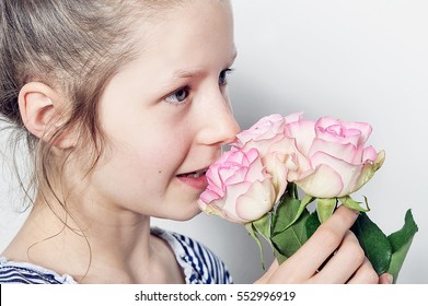 Young Girl Is Smelling With Her Nose At Beautiful Pink Rose Flowers