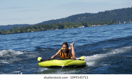 A young girl smiles while being pulled on an inner tube behind a boat on sunny day on Lake Washington near Seattle in Washington state.

