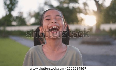 A young girl is smiling and laughing while standing in a park. Concept of happiness and joy, as the girl's laughter is contagious and uplifting
