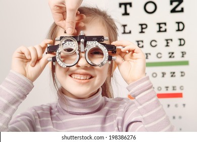 Young girl smiling while undergoing eye test with phoropter - Powered by Shutterstock