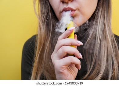 Una niña fuma un cigarrillo electrónico desechable. Fondo amarillo brillante