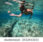 Young girl snorkeling with marine life underwater, in the clear warm ocean with rocky seabed. Travel picture with the woman snorkeler in the sea. Turquoise water and swimming tourist. 