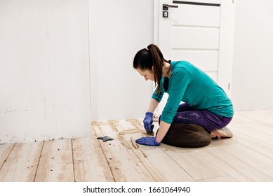 young girl spits on the floor,home repair work,smiling woman putstles the floor and holds a spatula in her hands,filling the wooden floor