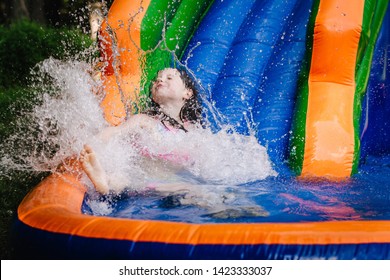 Young girl splashing into the bottom of a water bouncy slide.