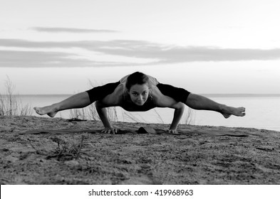 Young girl in sport wear making yoga on the seaside. Exercises on the sand. Upavistha konasana pose in sunset time. Black and white picture.