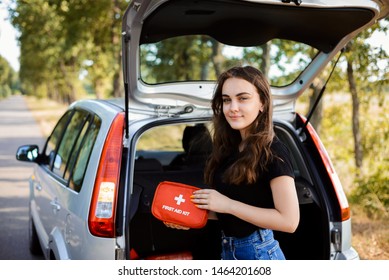Young girl standing near open back door of silver hatchback car and shows first aid kit that must be in every car for emergency - Shutterstock ID 1464201608