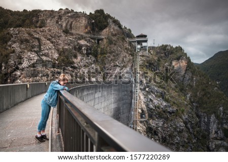 Young girl standing on massive Gordon dam water reservoir in Tasmania, admiring, looking below