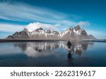 Young girl standing on the reflection of the sea water with the snow capped mountains of Stockness in the background. Iceland
