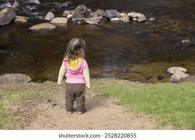 Young girl stands alone by a river, admiring the peaceful flow of water in nature. Her innocent curiosity and wonder capture the tranquility of childhood in a serene outdoor landscape - Powered by Shutterstock