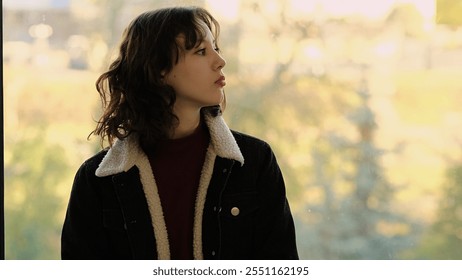 A young girl stands by a window, gazing thoughtfully at the bright outdoor scenery. This image captures themes of introspection, connection to nature, and quiet reflection. - Powered by Shutterstock